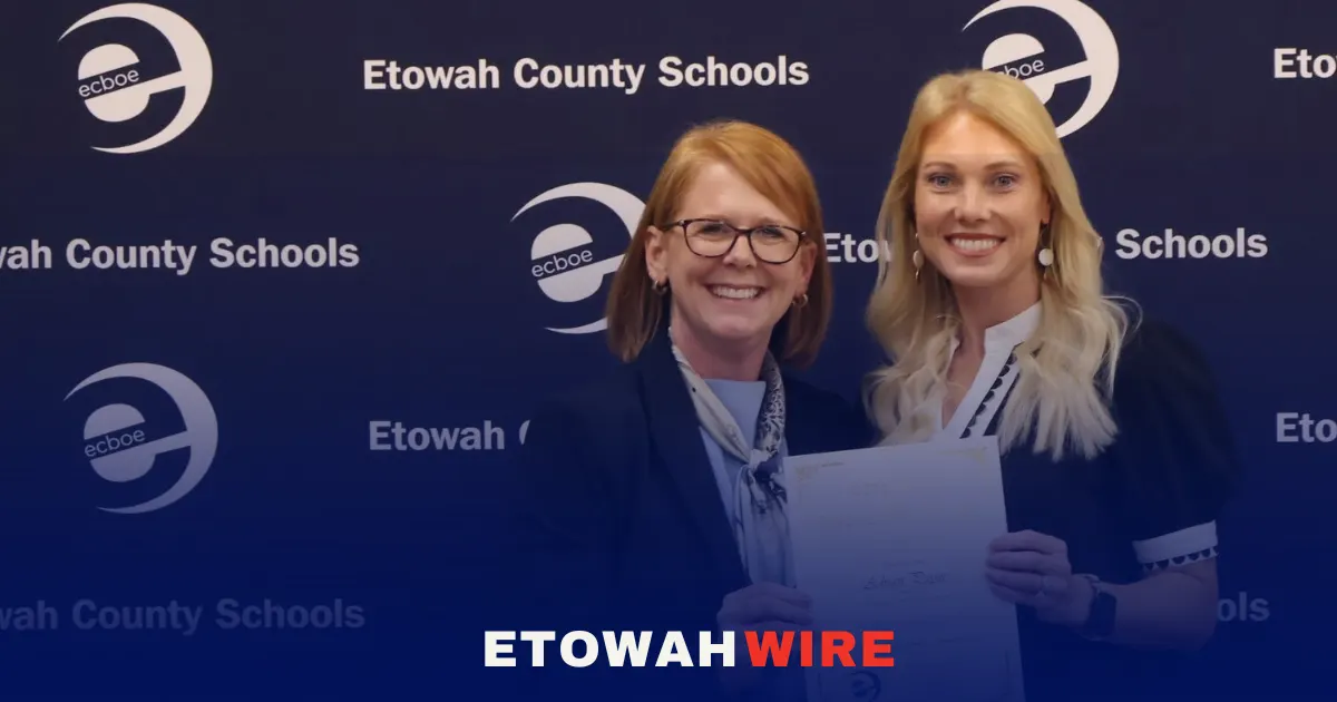 Two women stand together holding a certificate in front of an Etowah County Schools backdrop.